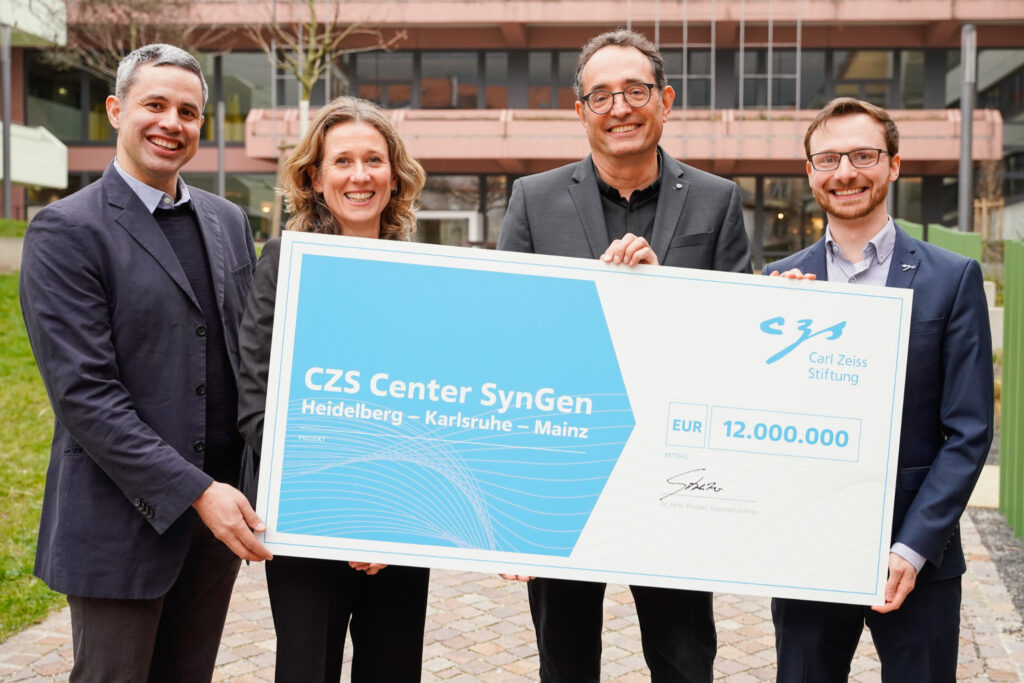 Professor Michael Knop (second from right), spokesperson of the new CZS Center SynGen, together with the other two members of the management committee, Professor Sylvia Erhardt (second from left) and Professor Edward Lemke (left) as well as Dr. Phil-Alan Gärtig (right), who handed over a symbolic cheque on behalf of the Carl-Zeiss-Stiftung (photo/©: Uwe Anspach / Heidelberg University)