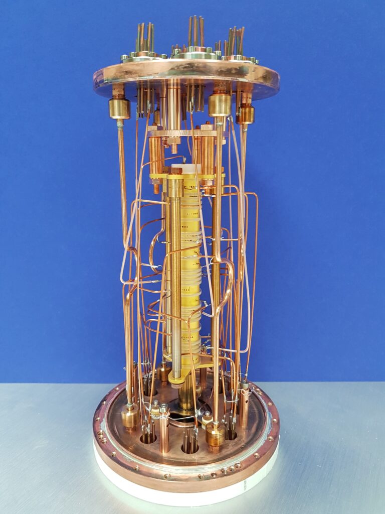 An extremely precise atomic balance: PENTATRAP consists of five Penning traps arranged one above the other (yellow tower in the middle). In these identically constructed traps, ions in the excited quantum state and in the ground state can be measured in comparison. In order to minimize uncertainties, the ions are also moved back and forth between different traps for comparative measurements. (© Max Planck Institute for Nuclear Physics)